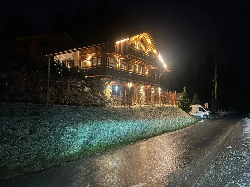 Façade de chalet éclairée la nuit, balcons soulignés de lumière